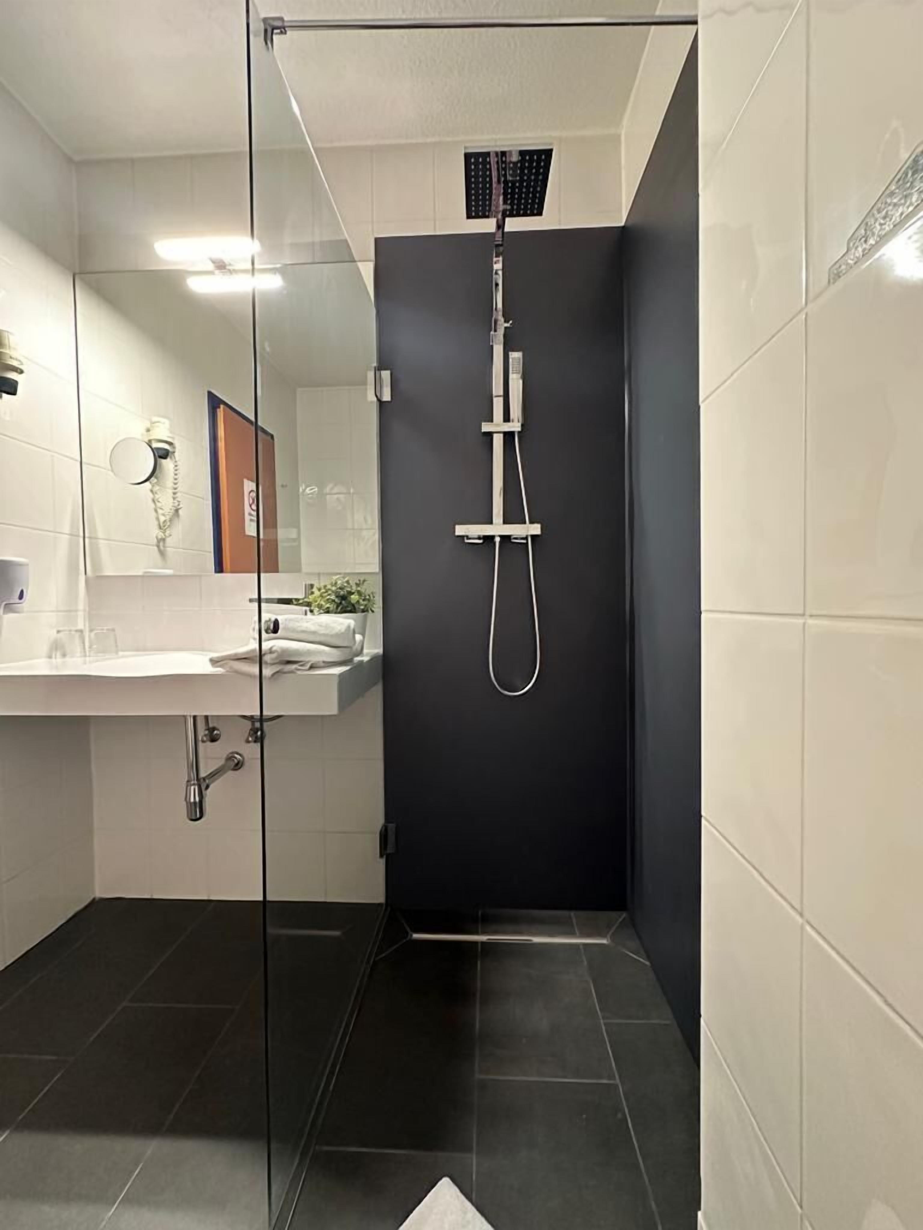 A modern bathroom with a glass-enclosed shower, white tiles, and a dark accent wall.