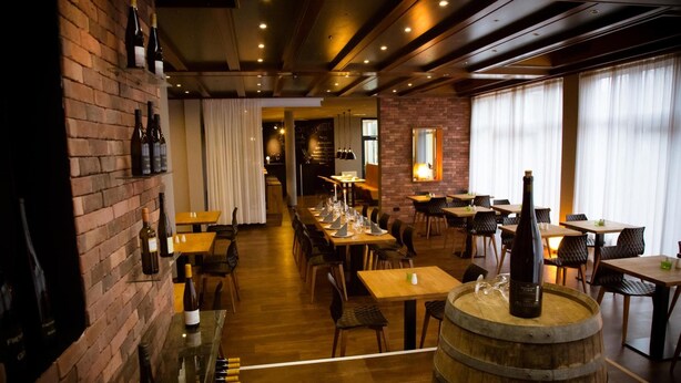 A restaurant with brick walls, wooden tables, and a bar area with wine bottles. - Rheinhessen Inn (Woerrstadt)