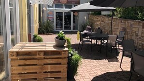 An outdoor patio area with wooden planters, a table and chairs, and a large umbrella. - Rheinhessen Inn (Woerrstadt)