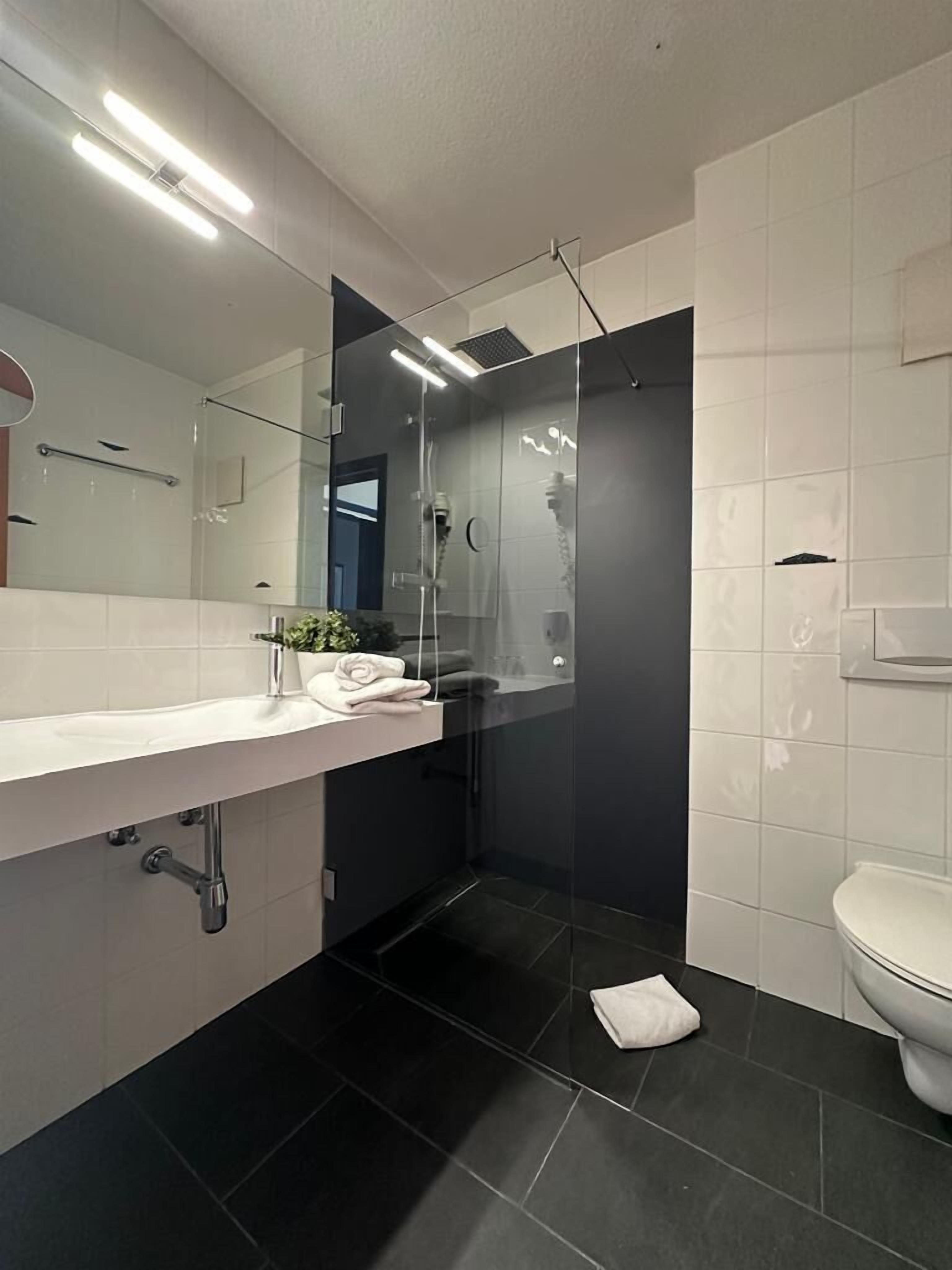 Un baño moderno con ducha de vidrio, lavamanos blanco con una toalla y un inodoro.