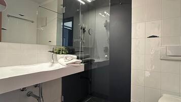 Un baño moderno con ducha de vidrio, lavamanos blanco con una toalla y un inodoro.