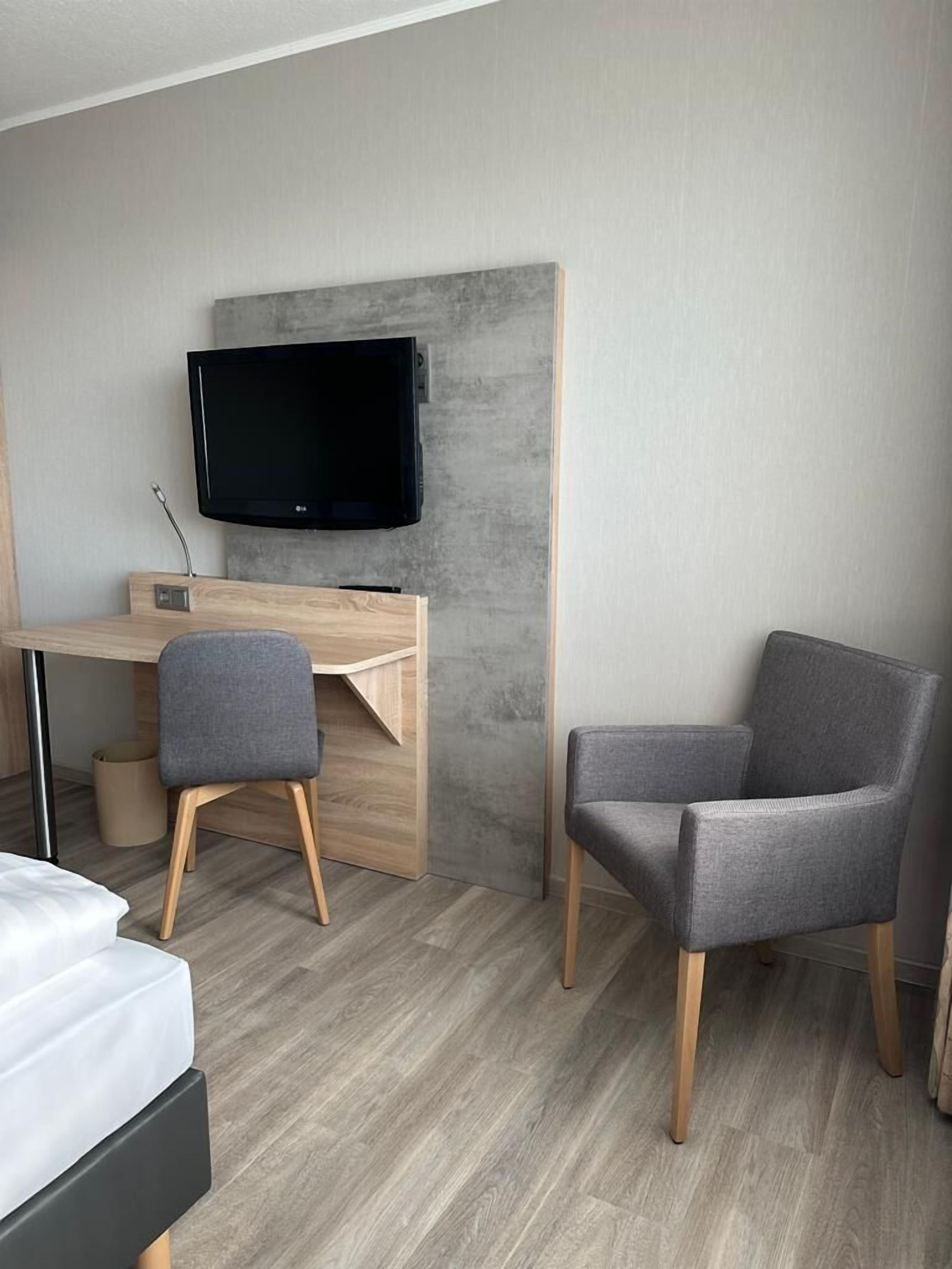 A modern hotel room with a wooden desk, a grey office chair, a television, and a bed.