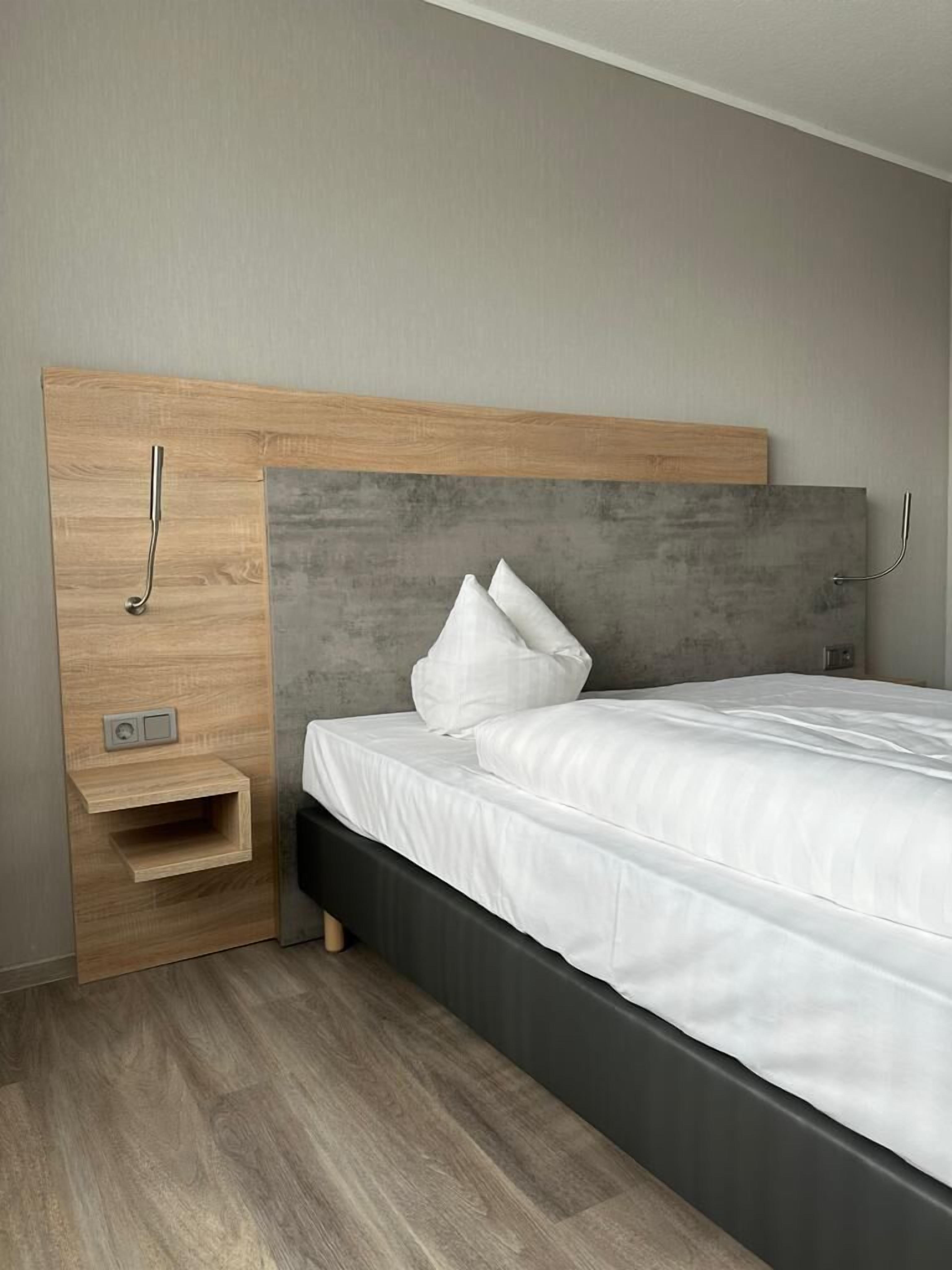 A modern bedroom with a wooden headboard, a bedside table, and a bed with white bedding.