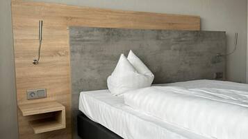A modern bedroom with a wooden headboard, a bedside table, and a bed with white bedding.
