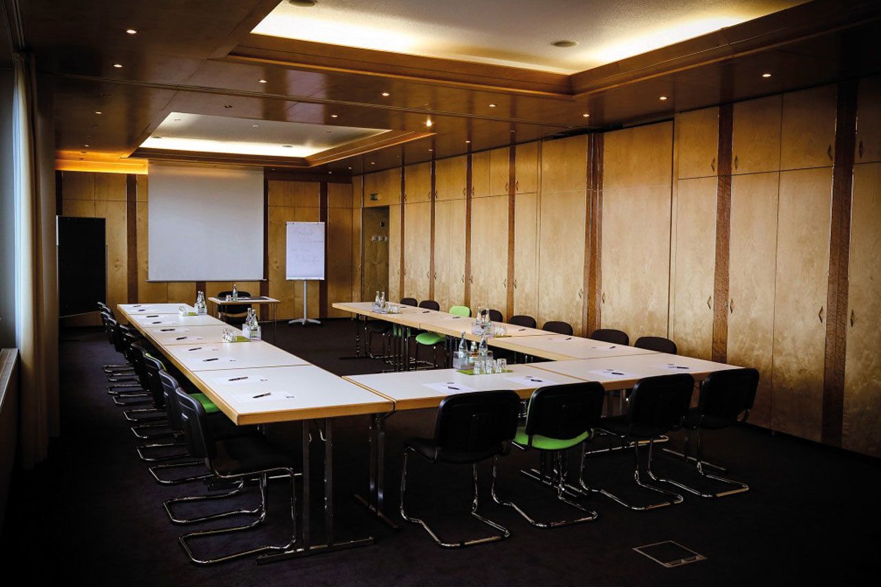 A conference room with long tables, chairs, a projector screen, and a whiteboard.