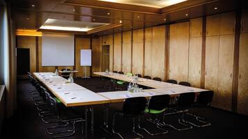 A conference room with long tables, chairs, a projector screen, and a whiteboard.