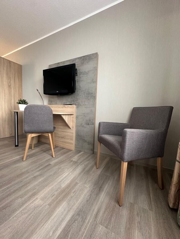 A modern room with a wooden desk, a grey upholstered chair, and a flat-screen TV mounted on a concrete wall.