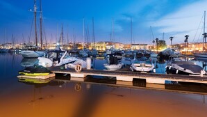 A marina at dusk with multiple boats docked, a wooden dock, and a cityscape in the background. - C06 - Porto do Mos 3 bed Townhouse by DreamAlgarve (Lagos)