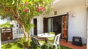 A patio with a table and chairs, a small tree with pink flowers, and a door leading to an interior space. - C06 - Porto do Mos 3 bed Townhouse by DreamAlgarve (Lagos)