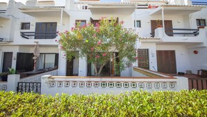 A white building with a balcony, a small garden with pink flowers, and a gate. - C06 - Porto do Mos 3 bed Townhouse by DreamAlgarve (Lagos)