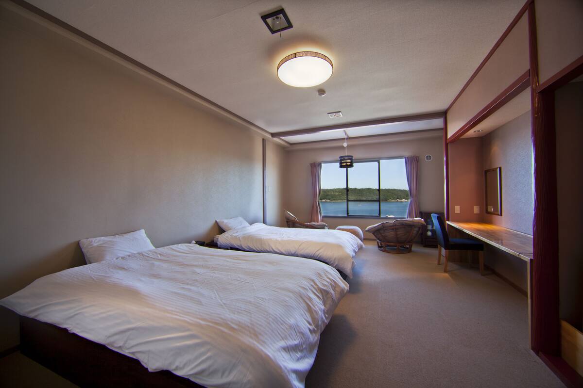 A hotel room with two beds, a desk, and a view of the sea.