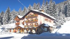 Ein mehrstöckiges Hotel mit einer Seilbahn im Hintergrund, umgeben von schneebedeckten Bäumen.