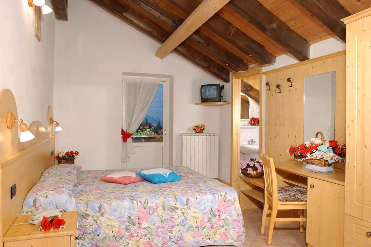 A bedroom with a wooden headboard, a bed with floral bedding, a wooden desk with a mirror, and a dresser.