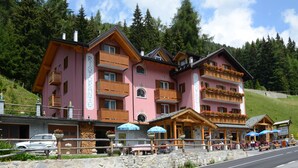 Ein pinkfarbenes Gebäude mit Balkonen, einer Bar und Außenbestuhlung.