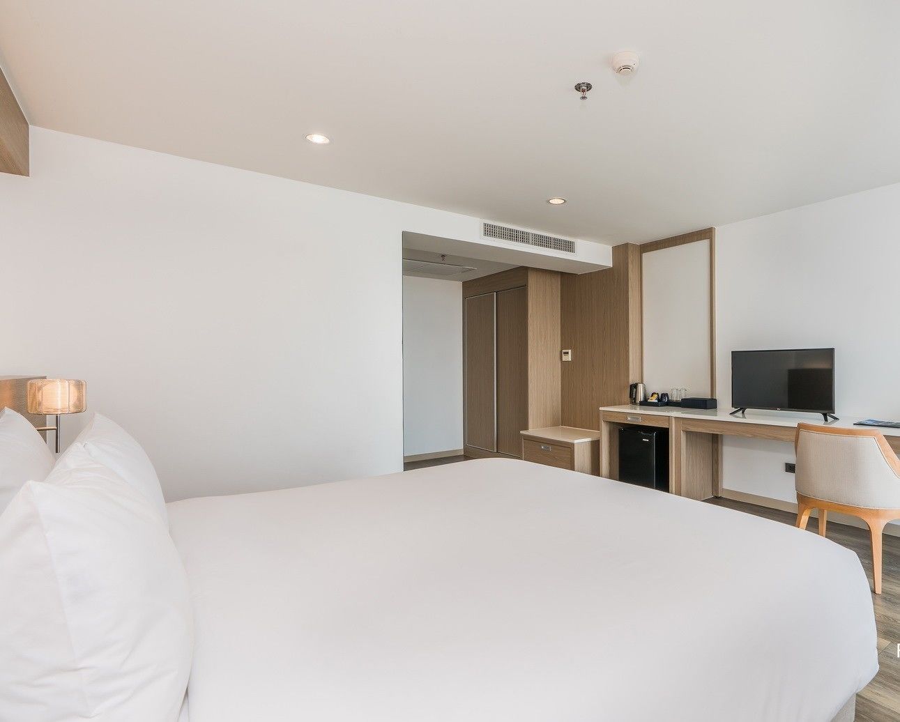 A hotel room with a large bed, a desk with a television, and a wardrobe.