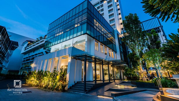 A modern hotel with a glass facade, outdoor seating, and a well-lit entrance. - Rattanachol Hotel (Chonburi)