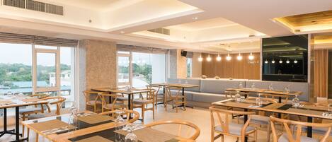 Un comedor moderno con varias mesas y sillas, ventanas amplias que ofrecen vistas a la ciudad y un diseño de techo contemporáneo.
