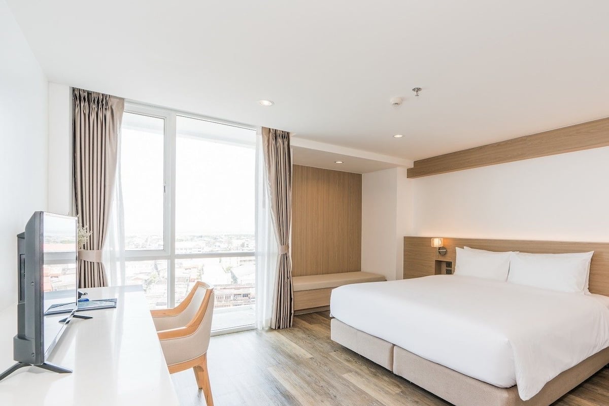 A hotel room with a bed, a desk, a chair, a TV, and a large window with curtains.