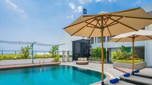 A rooftop pool area with a clear blue sky, a pool, lounge chairs, and umbrellas. - Rattanachol Hotel (Chonburi)