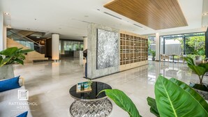 A spacious lobby with a marble wall, a wooden reception desk, and a staircase. - Rattanachol Hotel (Chonburi)