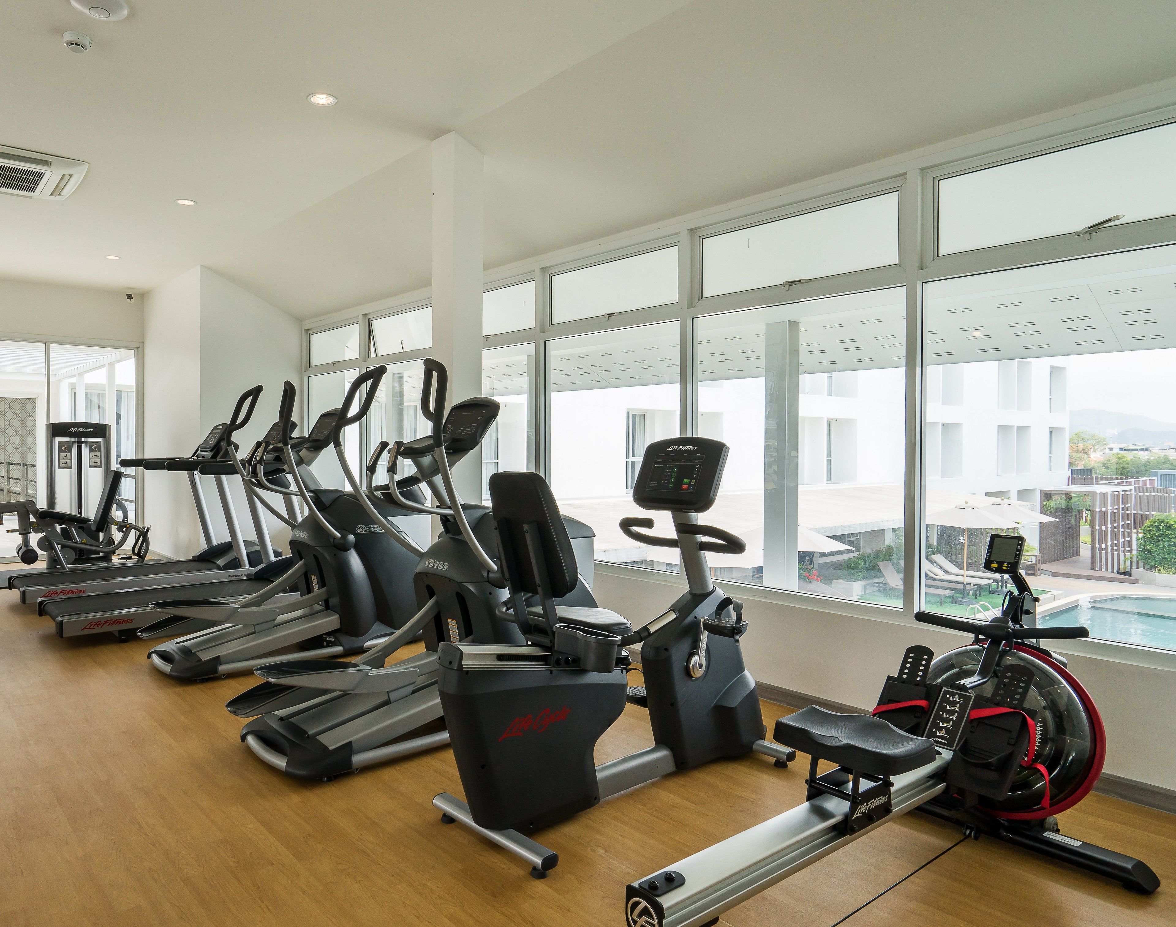 Un gimnasio con diversas máquinas de cardio, amplias ventanas y vistas al exterior.