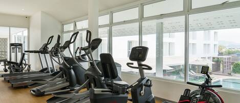 Un gimnasio con diversas máquinas de cardio, amplias ventanas y vistas al exterior.