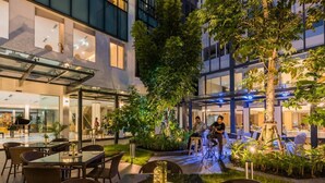 An outdoor dining area with tables and chairs, surrounded by greenery and a glass enclosure. - Rattanachol Hotel (Chonburi)