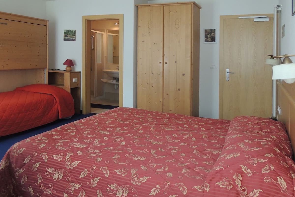 A bedroom with a large bed, two wooden wardrobes, a mirror, and a small bedside table with a lamp.