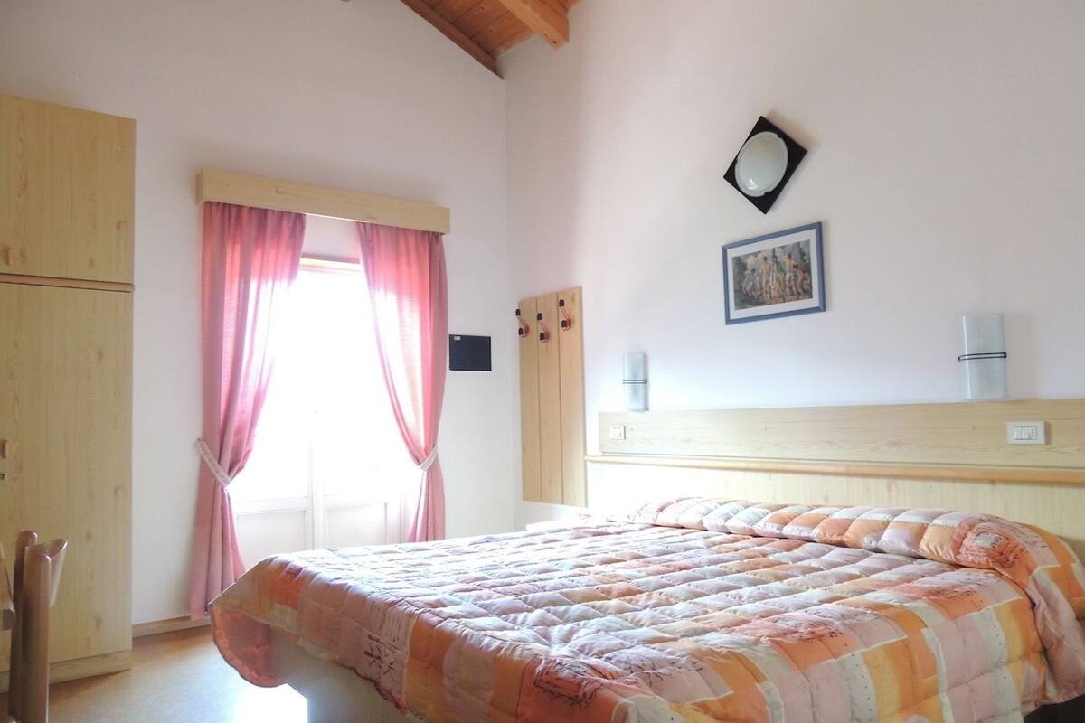 A bedroom with a bed, wooden wardrobe, and a window with curtains.