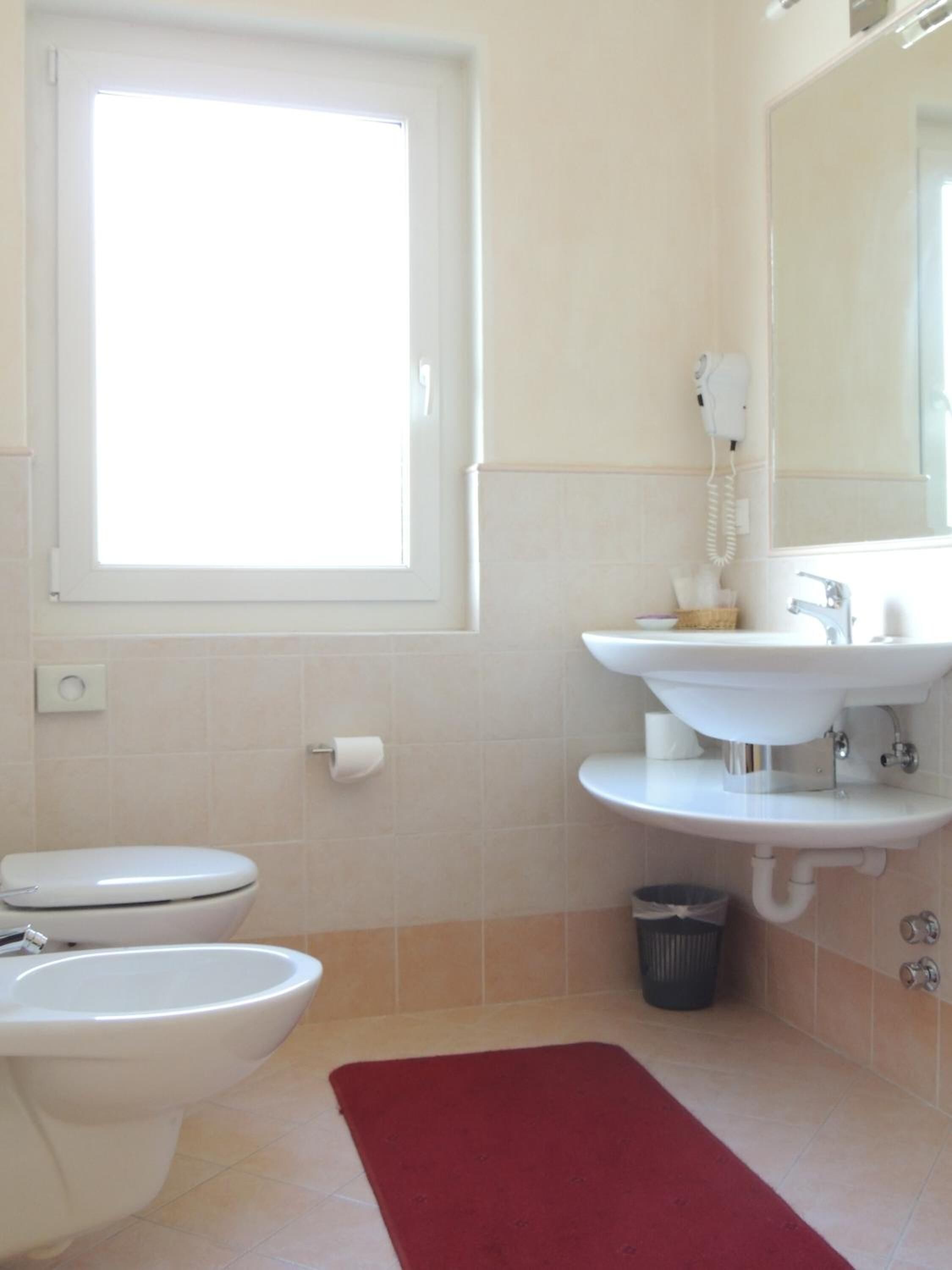 A bathroom with a toilet, bidet, sink, and a window providing natural light.