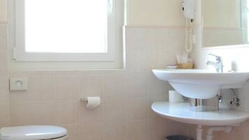 A bathroom with a toilet, bidet, sink, and a window providing natural light.