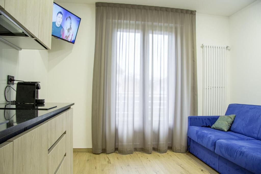Une pièce dotée d’une kitchenette, d’un canapé bleu et d’un téléviseur fixé au mur.