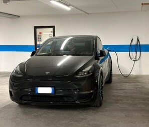 A black Tesla charging in a parking garage with a blue stripe on the wall.