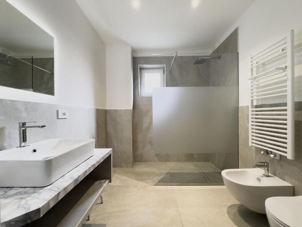 Une salle de bain moderne avec un grand miroir, un lavabo sur pied, un bidet et un espace douche.