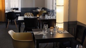 Un comedor de hotel con mesas dispuestas para dos, equipado con copas de vino, vasos de agua y cubiertos.