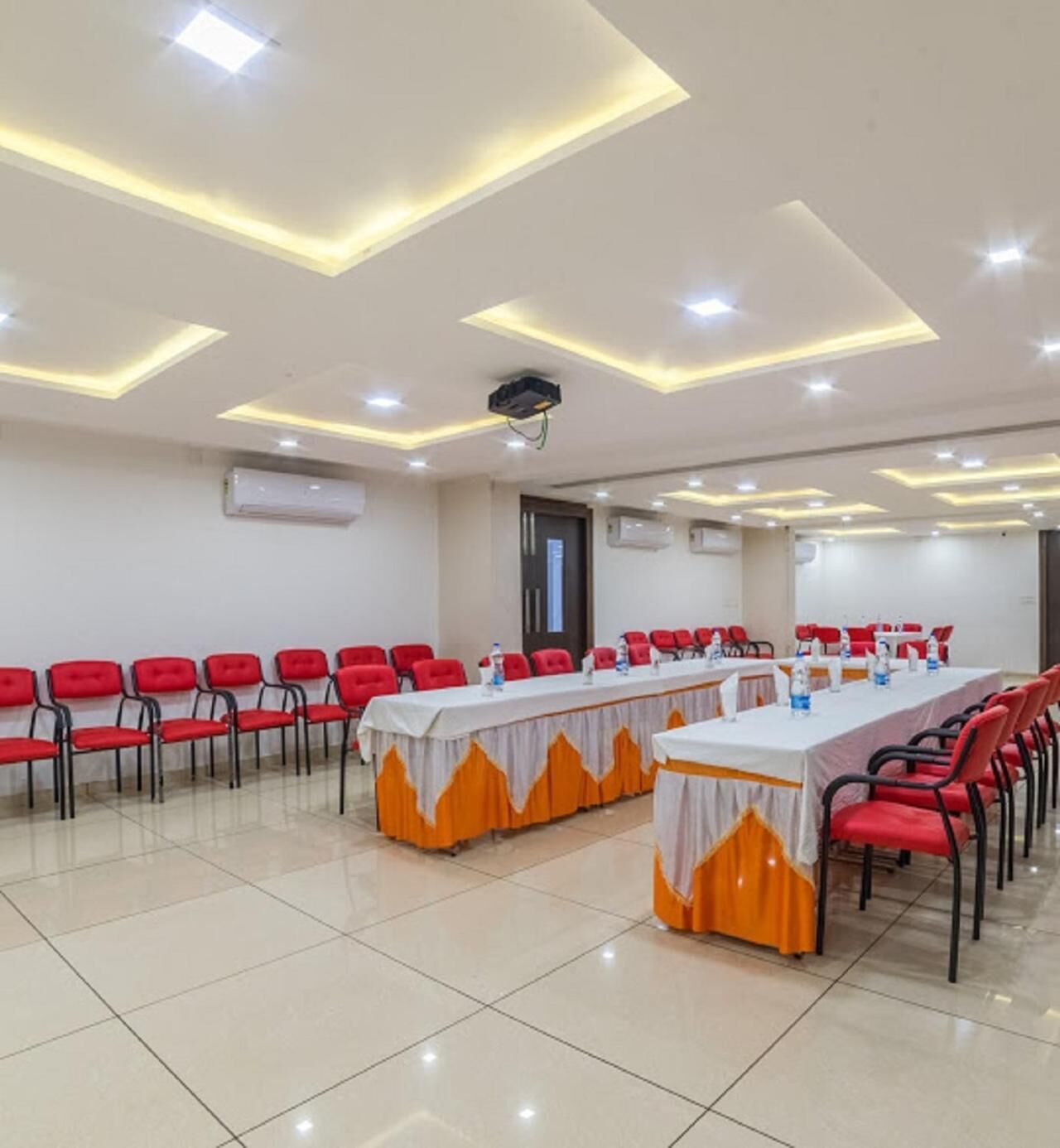 Una sala de conferències amb una taula llarga, cadires vermelles i un projector al sostre.
