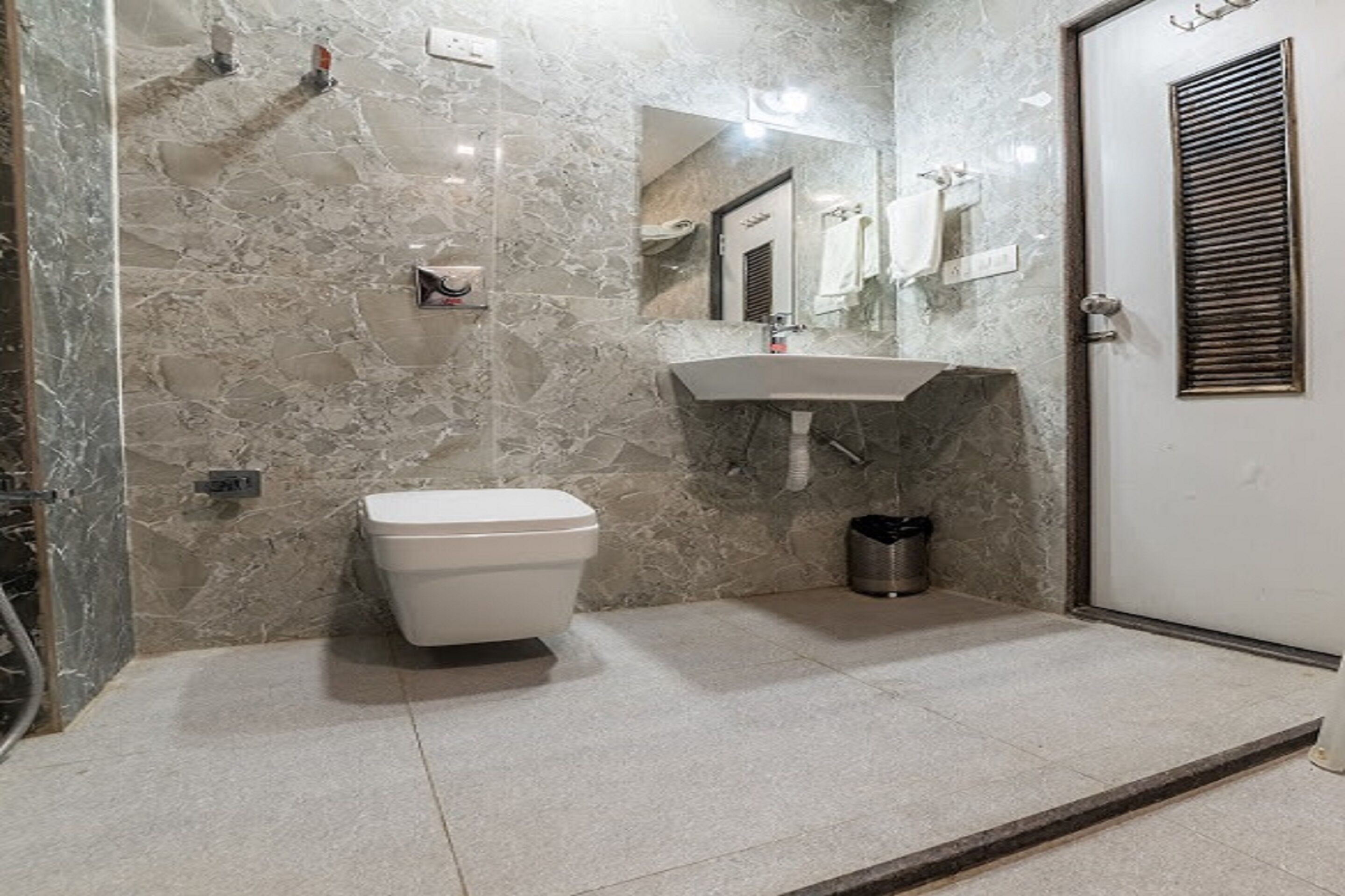 A bathroom with a marble wall, a toilet, a sink, and a door with a window.