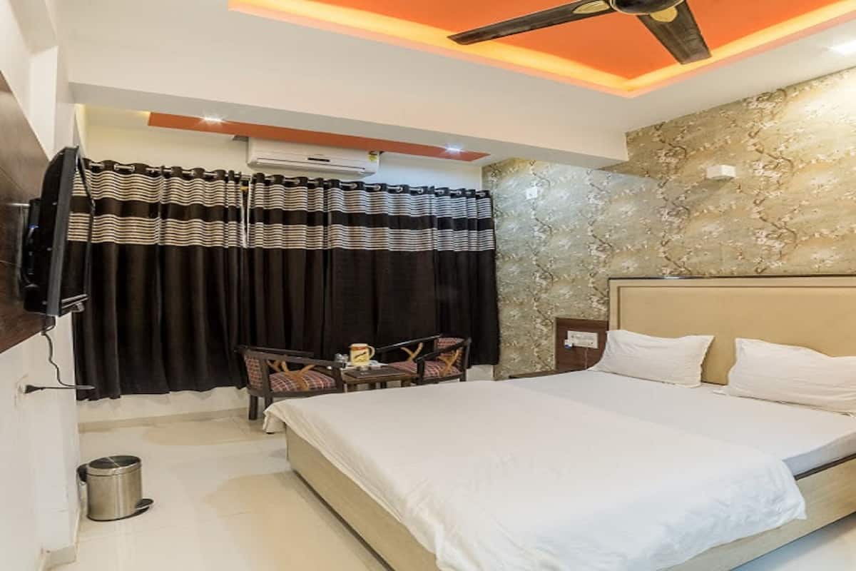 Ein Hotelzimmer mit Bett, Wandfernseher, einem kleinen Tisch mit Stühlen und Deckenventilator.