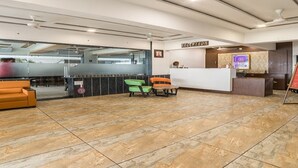 Un espace d’accueil comprenant un comptoir de réception, un fauteuil vert et orange, et un panneau indiquant « Réception ».