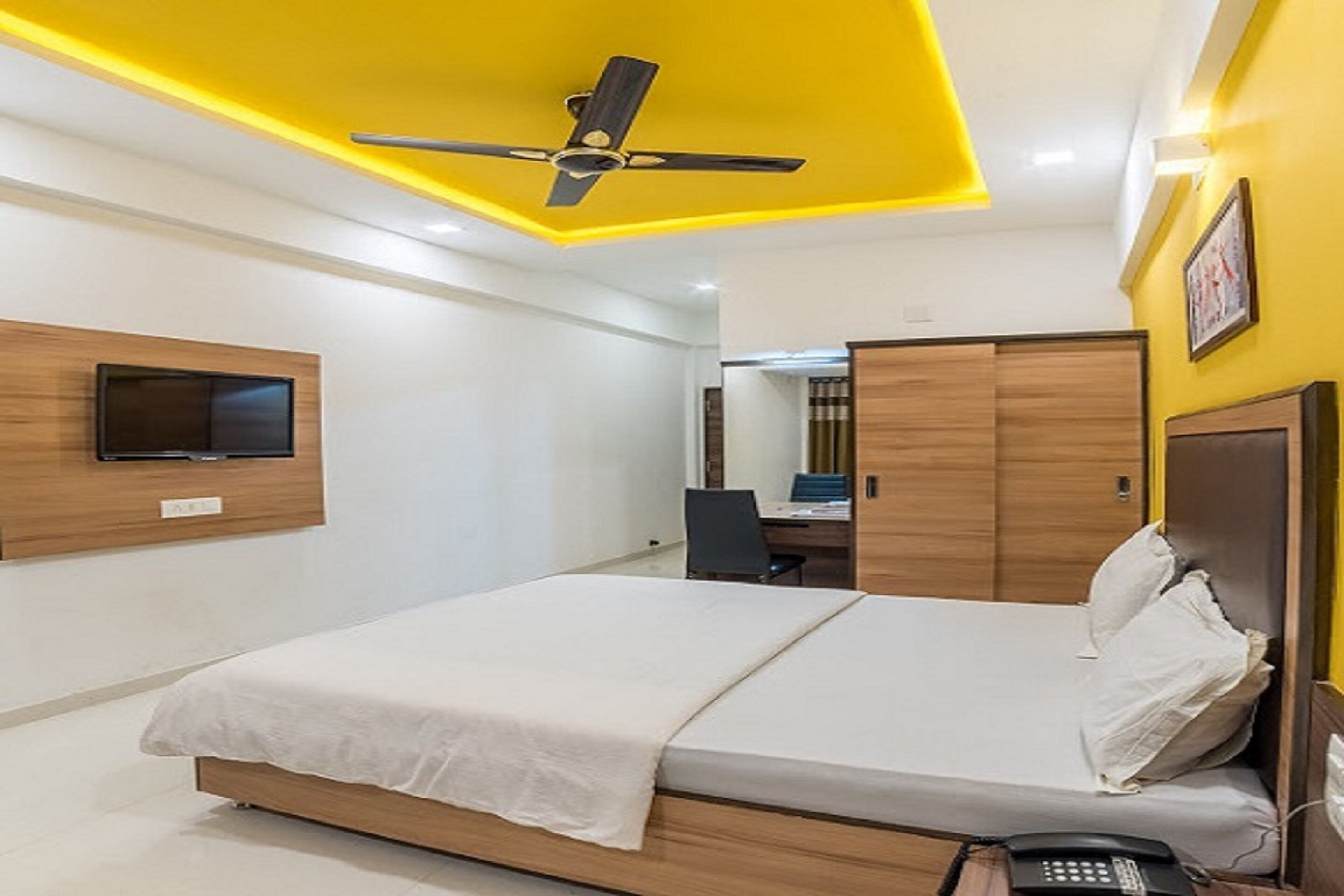 Een hotelkamer met een bed, een bureau, een stoel, een telefoon en een plafondventilator.