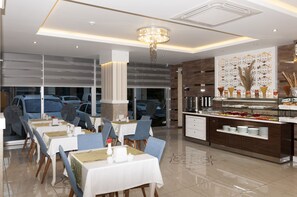 A modern dining area with tables set for service, a buffet station, and a decorative wall with a tree motif. - Park Yalcin Hotel (Mersin)