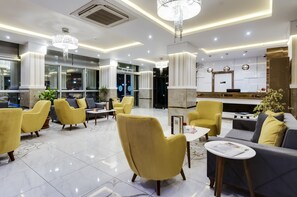 Un moderno vestíbulo de hotel con sillones amarillos, un sofá gris, una recepción y una araña.