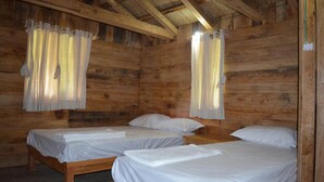 A cabin with two wooden beds, each with white linens, and curtains hanging from the ceiling. - Kalsee Ecolodge (Lumle)