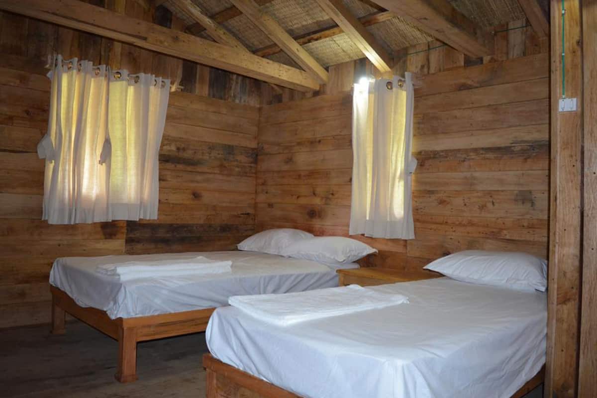 A cabin with two wooden beds, each with white linens, and curtains hanging from the ceiling.