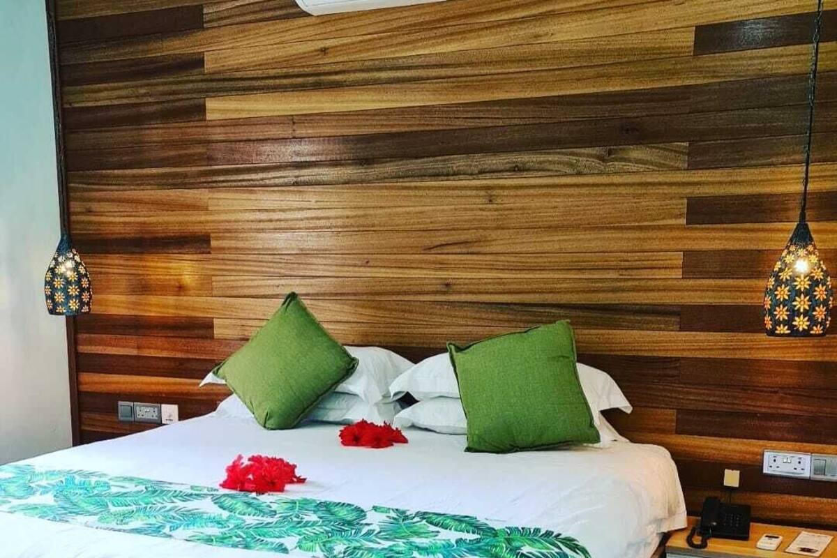A neatly made bed with a white and green patterned bedspread, two green pillows, and a red flower on the bed.