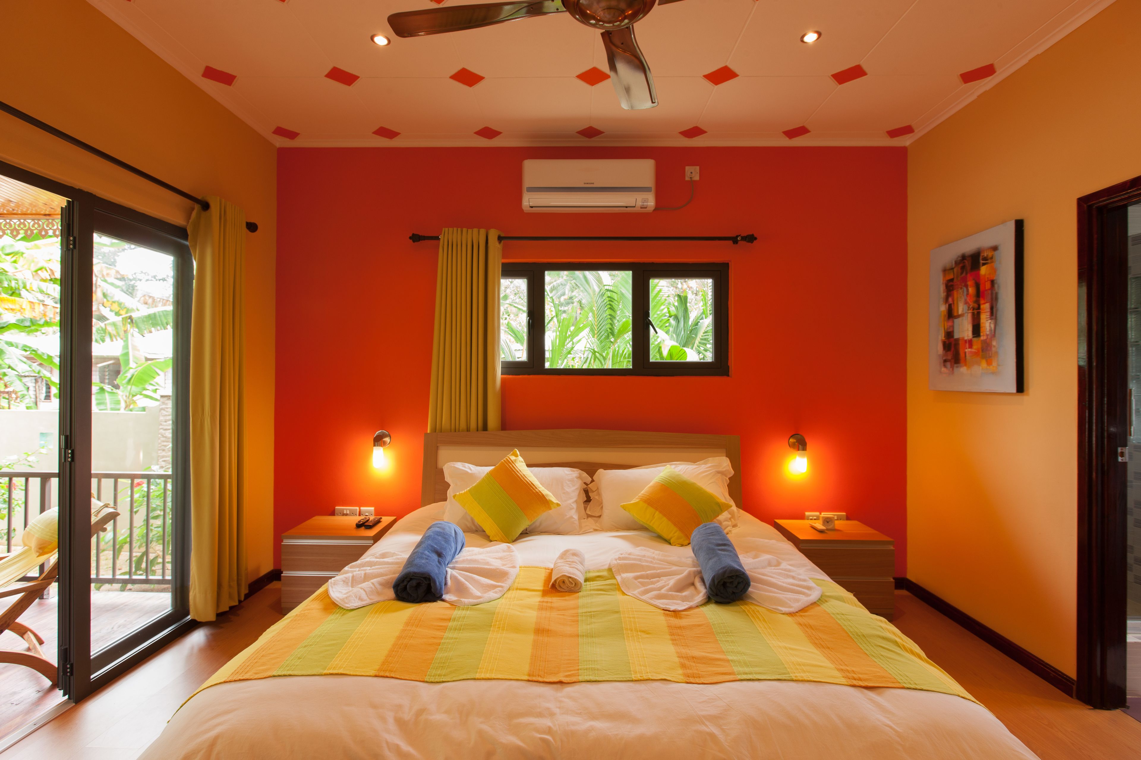 Ein Hotelzimmer mit einem Bett, zwei Nachttischen, einer Klimaanlage, einem Deckenventilator und einem Fenster mit Vorhängen.