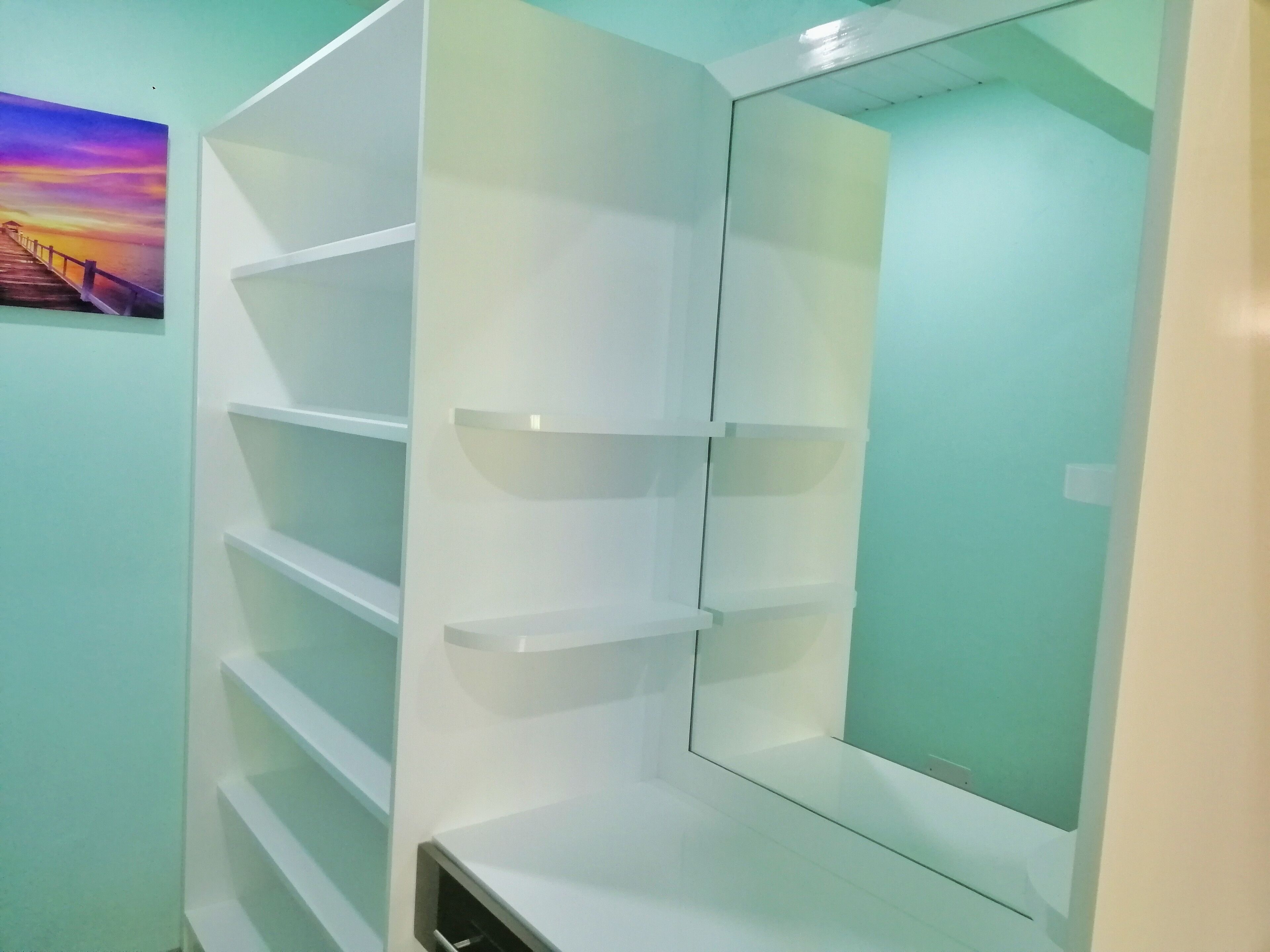 A corner of a room with white shelving units and a large mirror.
