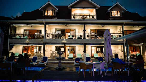Un hotel de dos pisos con piscina, zona de estar al aire libre y una entrada bien iluminada.