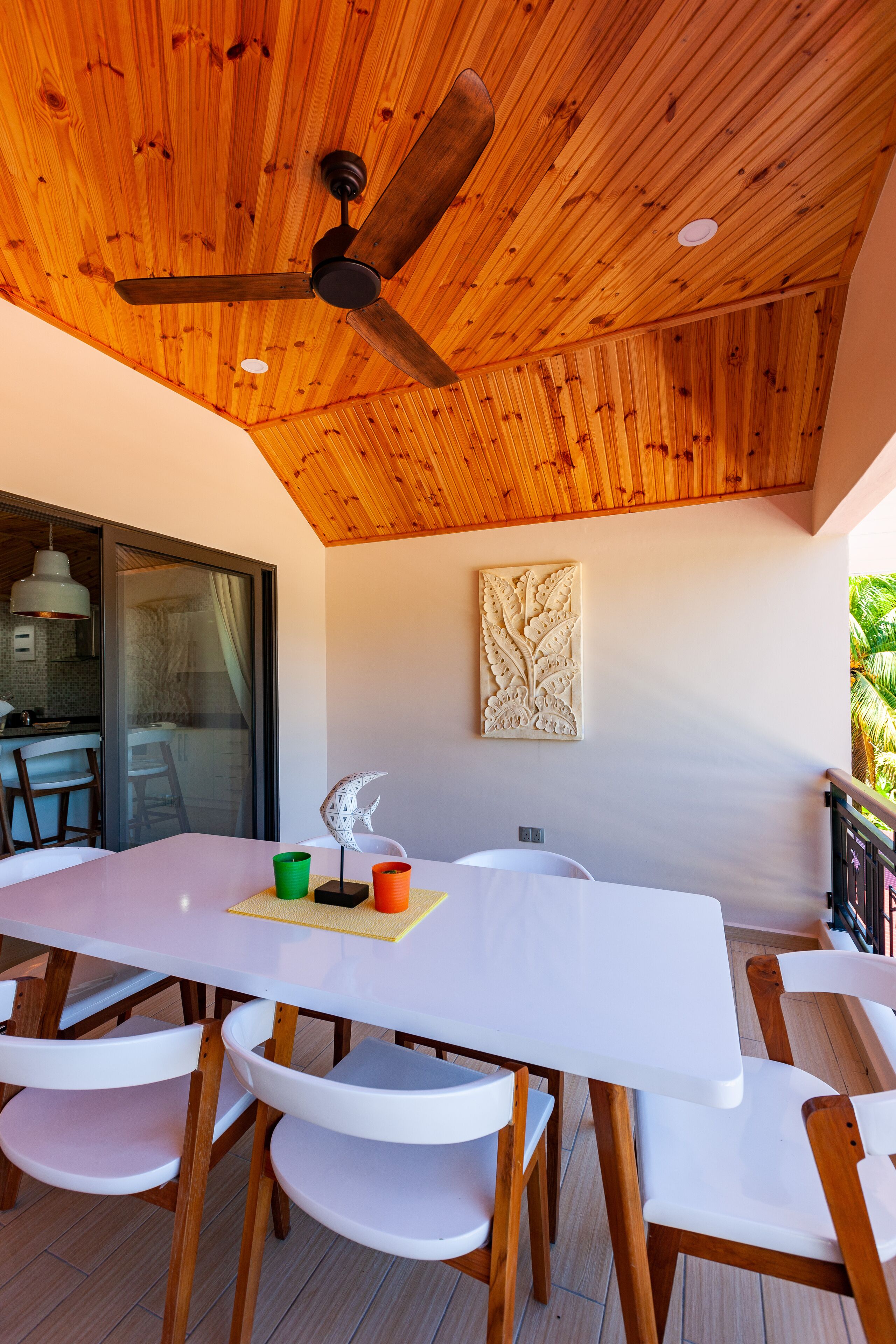 A dining area with a white table and chairs, a ceiling fan, and a decorative wall piece.