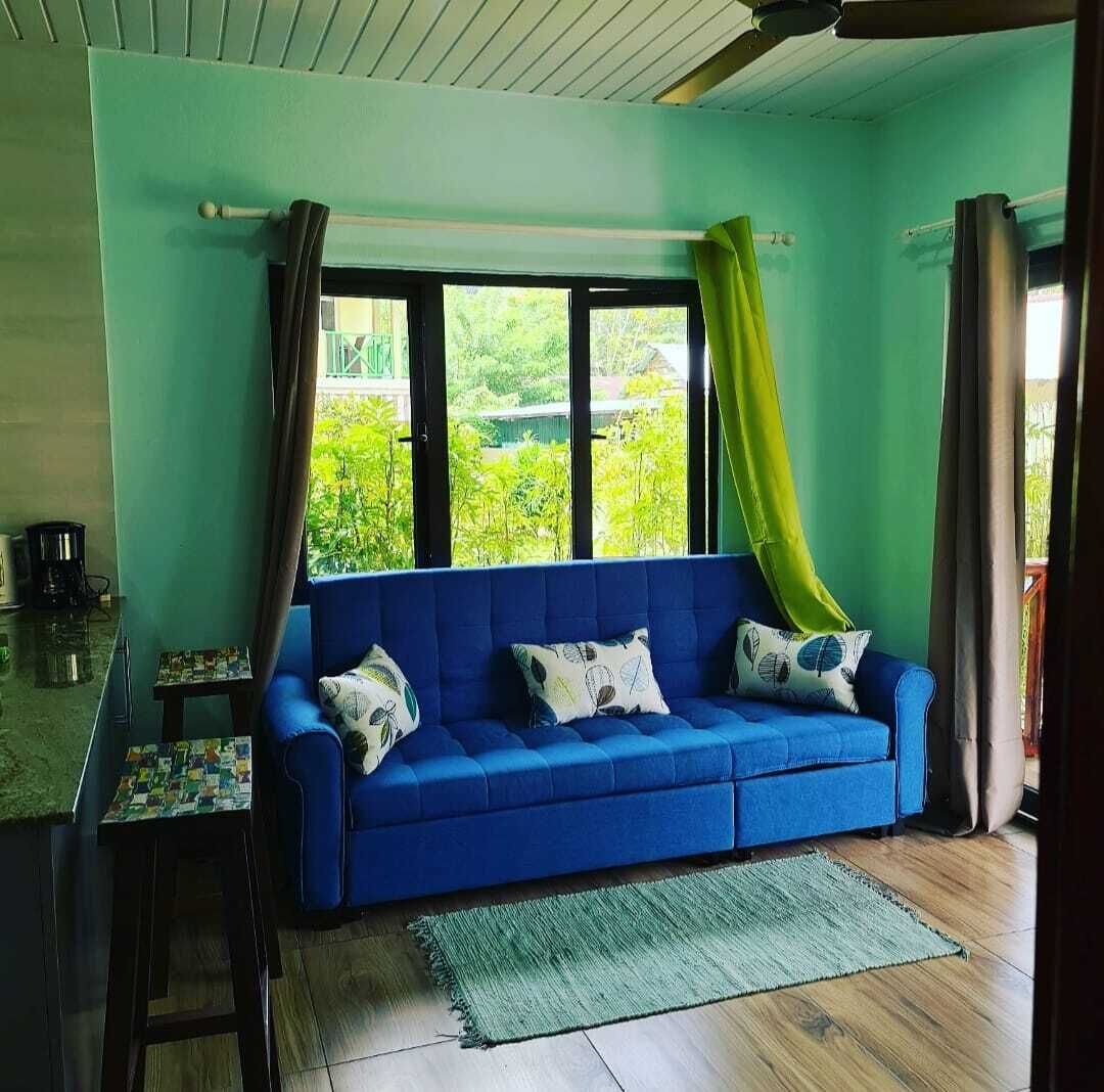 A blue sofa with patterned cushions, a small table with a chessboard, and a green rug.